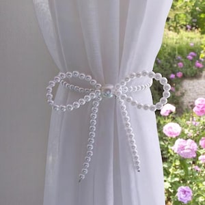 May include: White sheer curtains with a pearl tieback. The tieback is a bow made of a string of pearls.