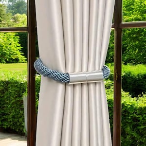 May include: A blue rope curtain tieback with silver metal ends. The tieback is holding back a set of white curtains.