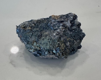May include: A dark gray and silver rock with a rough, uneven surface. The rock has a metallic sheen and appears to be made of multiple minerals.