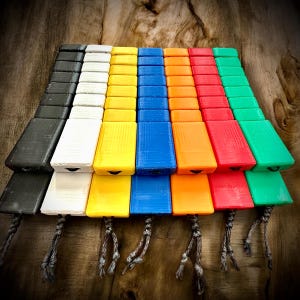 May include: A collection of colorful, rectangular objects arranged in rows. The objects are in various colors, including black, white, yellow, blue, orange, red, and green. Each object has a small opening and is attached to a braided cord.