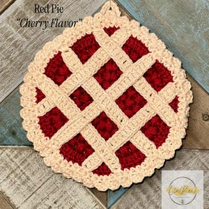 May include: A handmade crochet pie-shaped item with a red filling and a lattice crust. The crust and lattice are a light beige color, and the filling is a deep red. The text "Red Pie" and "Cherry Flavor" are visible at the top.