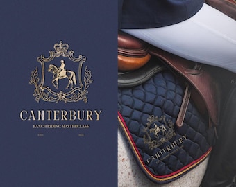 Op de afbeelding: Een donkerblauwe zadeldeken met gouden borduurwerk met een paard en ruiter. De zadeldeken heeft een rode en gouden bies en de tekst "Canterbury Ranch Riding Masterclass" is op de deken gedrukt.