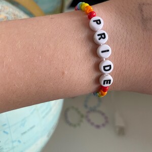May include: A rainbow beaded bracelet with white beads that spell out "PRIDE".