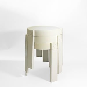 Può includere: Uno sgabello geometrico beige chiaro con un piano circolare e gambe rettangolari. Lo sgabello ha un design moderno con un aspetto a strati. Lo sgabello è realizzato in un materiale solido ed è adatto per uso interno.