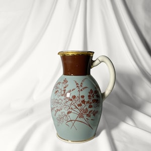 Peut inclure: Un pichet en céramique bleu et brun avec un motif floral. Le pichet a un bord et une poignée dorés.