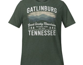 以下が含まれることがあります： 「Gatlinburg」の文字、山脈、そして「Great Smoky Mountains National Park Est. 1934 Tennessee」という文字が描かれた、ヴィンテージスタイルのグラフィックデザインが施された濃い緑色のTシャツです。