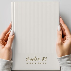 Puede incluir: Un libro de tapa dura blanco con un sutil patrón de rayas verticales. La portada presenta el texto "chapter 80" en una fuente cursiva sobre el nombre "OLIVIA SMITH" impreso en una fuente de letras mayúsculas sin remates.