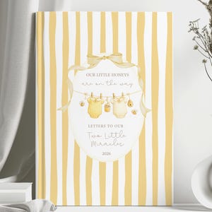 May include: A hardback book with a yellow and white striped cover. The cover features a decorative label with the text "OUR LITTLE HONEYS are on the way" and "Letters to our Two Little Miracles 2020". The label includes illustrations of baby clothes.