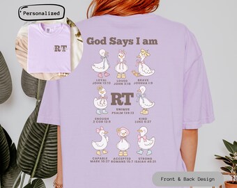 May include: A light purple t-shirt with a graphic of cartoon ducks, each with a different accessory. The text "God Says I am" is above the ducks, with various words like "Loyal" and "Brave" below them. The front of the shirt has the initials "RT".