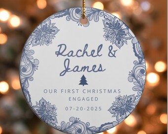 May include: A round, white Christmas ornament with a blue floral lace design around the edge. The ornament has the names "Rachel & James" and the text "OUR FIRST CHRISTMAS ENGAGED 07-20-2025" in blue script. A small Christmas tree graphic is also included.