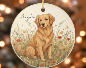 May include: Round ceramic ornament featuring a golden retriever illustration. The dog is seated in a field of wildflowers with the text "Axy's" in script. The ornament has a gold string for hanging.