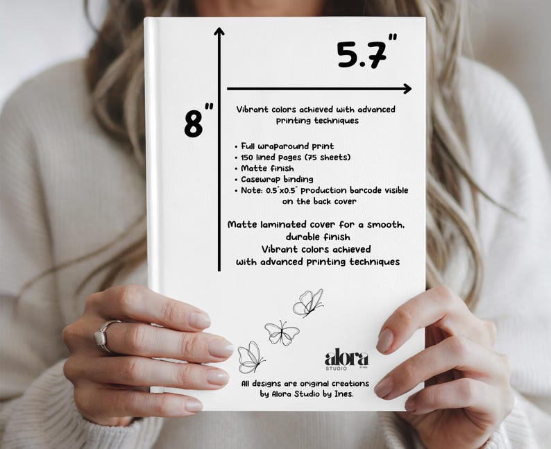 Puede incluir: Un cuaderno blanco con acabado mate, de 20,3 cm por 14,5 cm, sostenido por una persona. El cuaderno presenta un dise&ntilde;o de mariposa y el texto &laquo;Colores vibrantes logrados con t&eacute;cnicas de impresi&oacute;n avanzadas&raquo;. El cuaderno tiene 150 p&aacute;ginas rayadas.