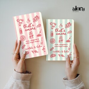 Puede incluir: Dos cuadernos con patrones de rayas verticales, uno rosa y otro verde menta. Cada cuaderno presenta la frase "that's amore" e ilustraciones con tem&aacute;tica de pasta. Tambi&eacute;n es visible el texto "Love, Laughter & Late-Night Pasta".