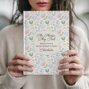 May include: A floral-patterned notebook with the text "The Things They Said" and "Notes from a Social Worker's Heart" is held up. The notebook has a light-colored background with pink, blue, and green floral designs.
