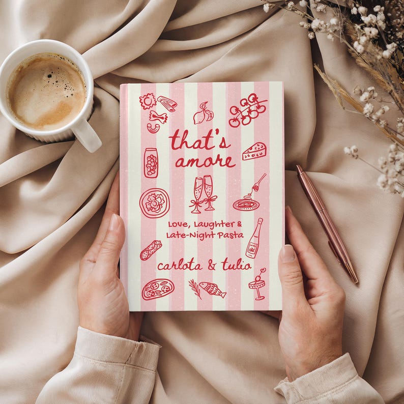 Puede incluir: Un cuaderno a rayas rosas y blancas con la frase "that's amore" e ilustraciones de comida italiana. El texto "Love, Laughter & Late-Night Pasta" y los nombres "carlota & tulia" tambi&eacute;n est&aacute;n presentes. Una taza de caf&eacute; y un bol&iacute;grafo tambi&eacute;n son visibles.