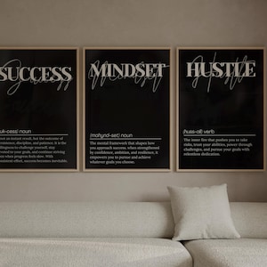 May include: Three vertical wall art prints in light wood frames featuring black backgrounds with white text. The prints display dictionary-style definitions for the words SUCCESS, MINDSET, and HUSTLE, each including phonetic spelling and descriptive text.
