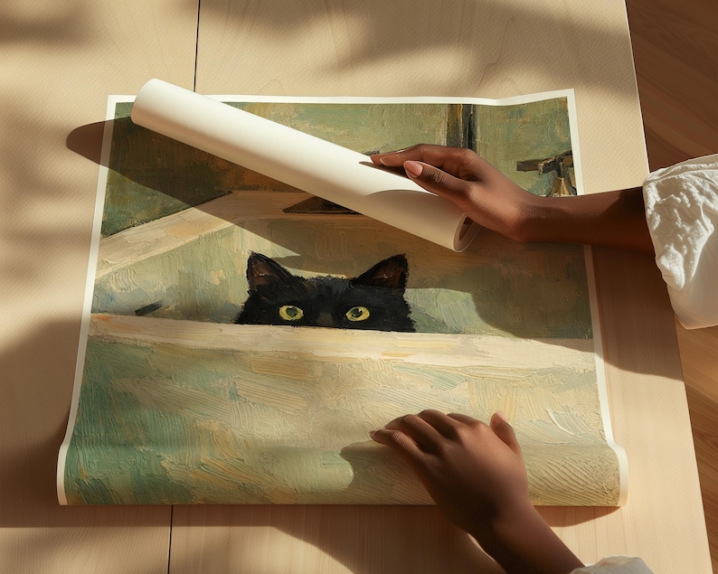 May include: A rolled white poster displaying a painting of a black cat with yellow eyes, peeking over a ledge. The artwork has a vintage aesthetic with muted green and beige tones. The poster is being held by two hands.