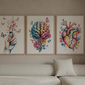 May include: Three framed watercolor art prints. One features a hand holding a syringe with flowers and butterflies. The second depicts a colorful brain with flowers and butterflies. The third shows a heart with flowers and butterflies.