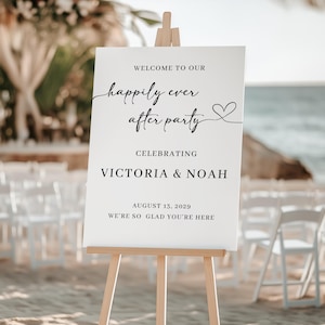 May include: A white sign on a wooden easel with the words "Welcome to Our Happily Ever After Party" in black script. The sign celebrates Victoria & Noah, with the date August 13, 2029, and the phrase "We're so glad you're here."