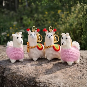 Könnte beinhalten: Vier handgefertigte Häkellama-Schlüsselanhänger. Zwei Lamas tragen rosa Pullover, und zwei haben bunte Satteldecken. Die Lamas haben goldene Schlüsselringe vor einem natürlichen Hintergrund.