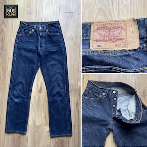 Könnte beinhalten: Dunkelblaue Jeans mit Knopfleiste. Die Jeans haben ein klassisches Fünf-Taschen-Design und einen Lederaufnäher mit dem Text "LEVI STRAUSS & CO." und "501". Die Bundweite ist W26 und die Länge L32.