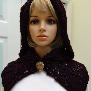 May include: A deep purple hooded cowl with a gold button closure. The cowl is made of a soft, knitted fabric and has a delicate, lacy pattern.