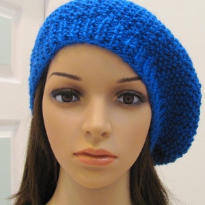 May include: A blue knitted beret with a textured pattern. The beret is worn on a mannequin with long brown hair.