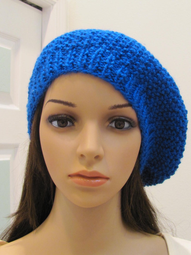 May include: A blue knitted beret with a textured pattern. The beret is worn on a mannequin with long brown hair.