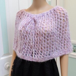 May include: A light purple crochet shawl with a delicate openwork pattern. The shawl is made of a soft, fuzzy yarn and has a slightly sheer appearance.