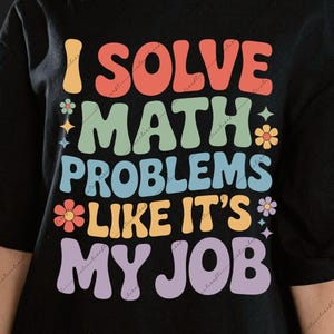 May include: Black t-shirt with the text "I Solve Math Problems Like It's My Job" in colorful, retro-style lettering. The design includes flowers and stars. A digital download file is available.
