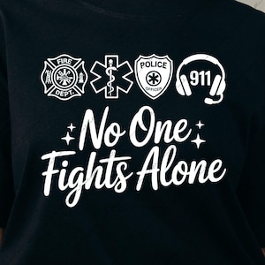 Puede incluir: Camiseta negra con gráficos y texto en blanco. El diseño incluye símbolos de bomberos, ambulancia, policía y 911, junto con las palabras "No One Fights Alone". Archivo de descarga digital.