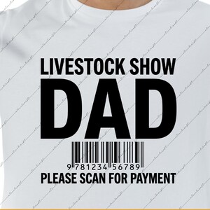 Könnte beinhalten: Ein weißes kurzärmeliges T-Shirt mit schwarzem Text, der LIVESTOCK SHOW DAD lautet, einer Strichcode-Grafik und dem Text PLEASE SCAN FOR PAYMENT. Das Design ist mittig auf der Brust des Kleidungsstücks platziert, das einen Rundhalsausschnitt hat.