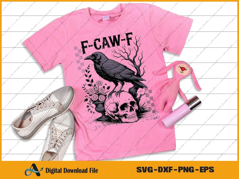 May include: Pink t-shirt with a graphic of a crow perched on a skull, with the text "F-CAW-F". The design includes a floral arrangement and a tree. Silver sneakers, a pink plush toy, and a pink tube are also in the image.