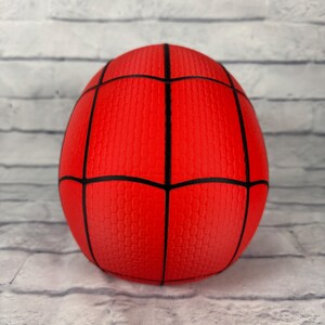 May include: A spherical red ball featuring a black web pattern across its surface. The ball has a textured finish with a repeating honeycomb-like pattern within each section created by the black lines, resembling a classic superhero costume design.