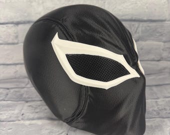 Op de afbeelding: Een zwart masker voor het hele hoofd met een getextureerd oppervlak en grote, hoekige witte oogframes. De oogopeningen zijn bedekt met een fijn zwart gaas, wat een duidelijk contrast vormt met de gladde, donkere afwerking van het masker.