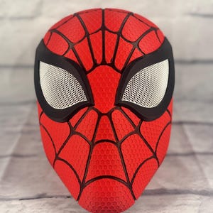 Puede incluir: Una m&aacute;scara de Spider-Man roja y negra con una superficie texturizada y una cubierta de malla para los ojos.
