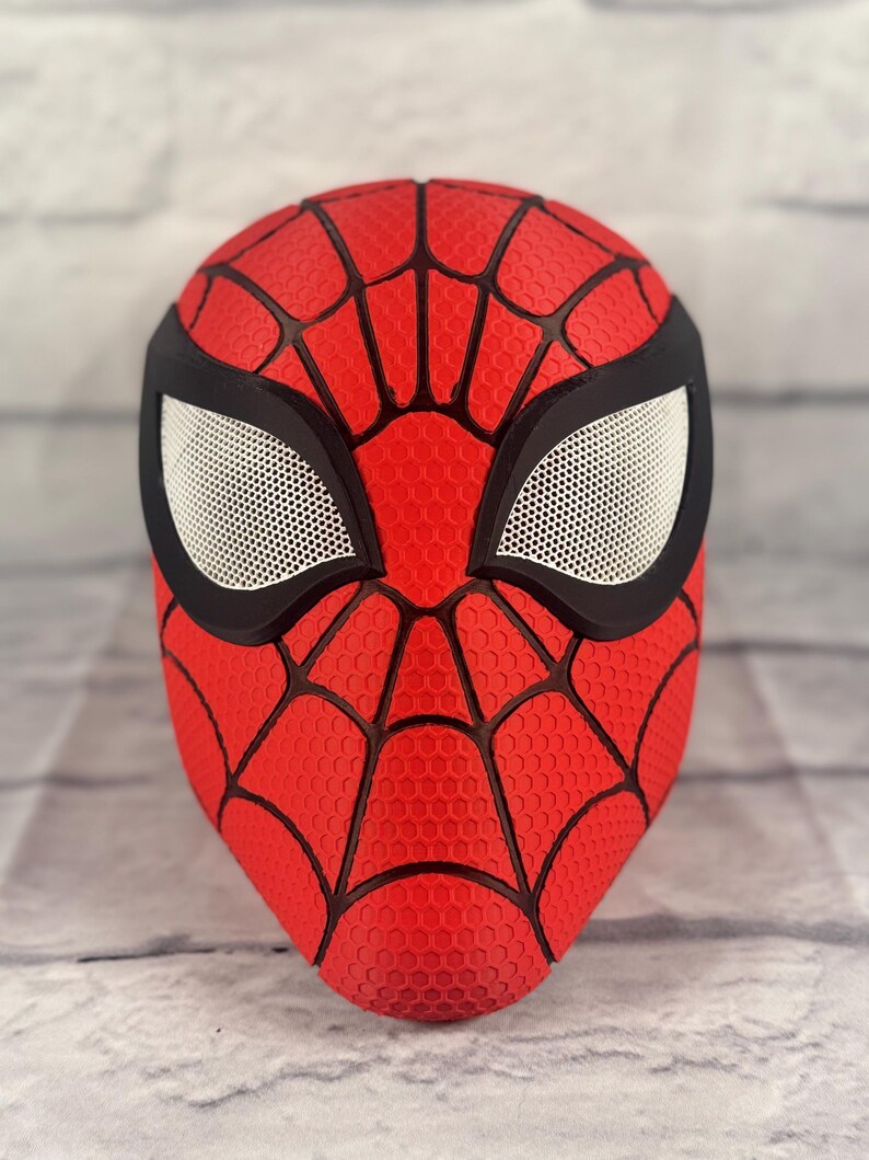 Puede incluir: Una m&aacute;scara de Spider-Man roja y negra con una superficie texturizada y una cubierta de malla para los ojos.