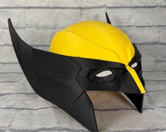 Op de afbeelding: Een geel en zwart superheldenmasker met een getextureerde koepel, puntige zijvinnen en witte mesh oogbedekkingen. Het ontwerp bevat een centrale gele streep over de neusbrug, met een matzwarte afwerking op het onderste gedeelte van het gezicht.