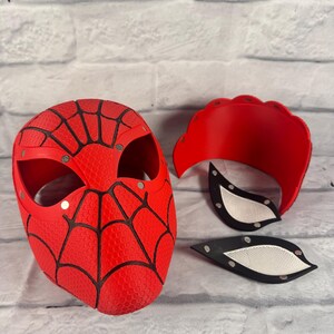 Puede incluir: Una m&aacute;scara de Spider-Man roja y negra con un dise&ntilde;o de telara&ntilde;a. La m&aacute;scara est&aacute; hecha de un material texturizado y tiene un dise&ntilde;o de telara&ntilde;a negra. La m&aacute;scara est&aacute; en tres piezas, con la m&aacute;scara principal, una pieza superior y dos piezas para los ojos.