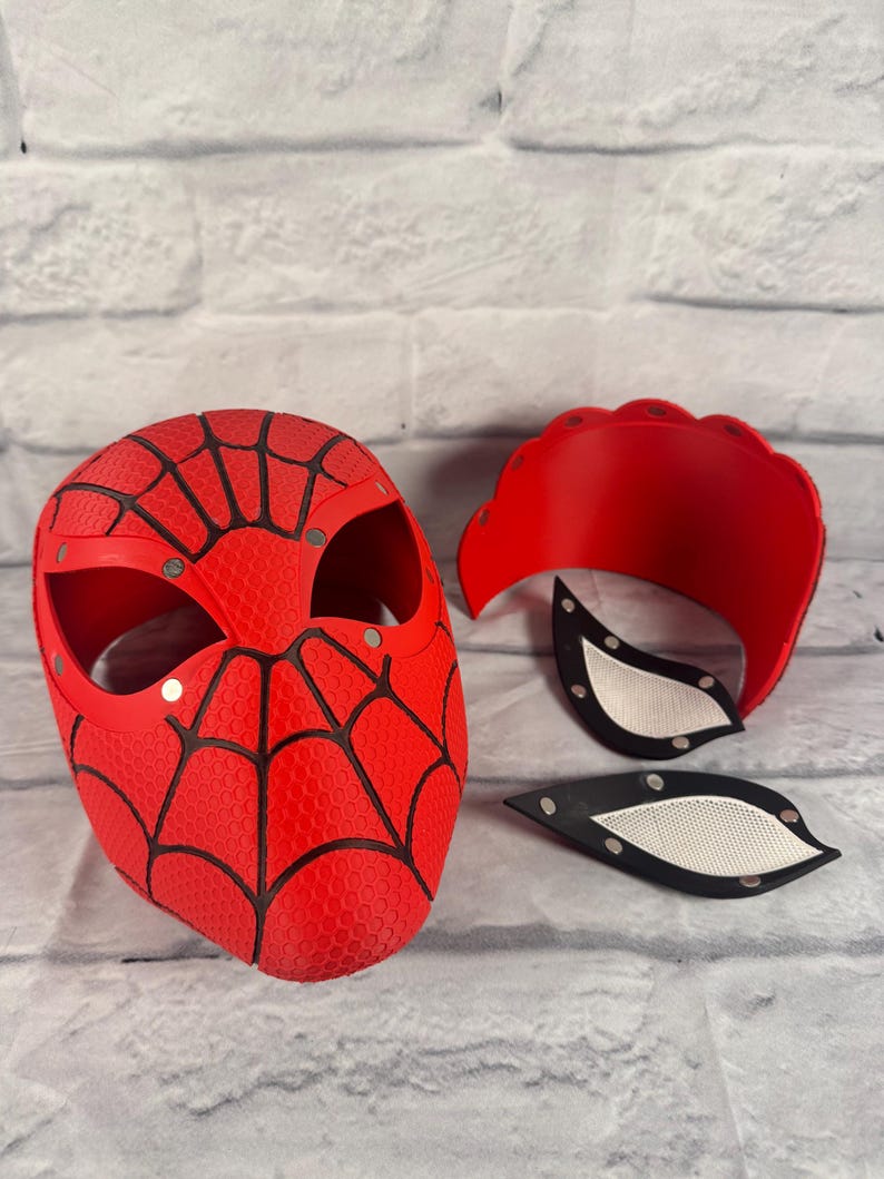 Puede incluir: Una m&aacute;scara de Spider-Man roja y negra con un dise&ntilde;o de telara&ntilde;a. La m&aacute;scara est&aacute; hecha de un material texturizado y tiene un dise&ntilde;o de telara&ntilde;a negra. La m&aacute;scara est&aacute; en tres piezas, con la m&aacute;scara principal, una pieza superior y dos piezas para los ojos.