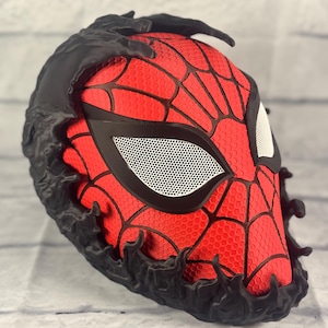 Puede incluir: Una m&aacute;scara impresa en 3D roja y negra con un dise&ntilde;o de telara&ntilde;a negra y un dise&ntilde;o de ara&ntilde;a negro texturizado alrededor de los bordes. La m&aacute;scara tiene una cubierta de ojo de malla blanca.