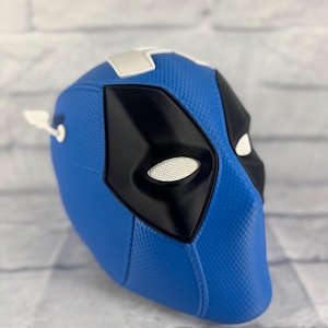 Könnte beinhalten: Eine blaue und schwarze Deadpool-Maske mit einem weißen Streifen oben. Die Maske besteht aus einem strukturierten Material und hat eine Netzaugenöffnung.