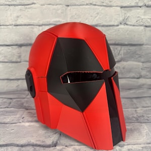 以下が含まれることがあります： 幾何学模様の赤と黒のヘルメット。ヘルメットは滑らかで光沢のある仕上がりで、黒色の顕著なバイザーエリアが特徴です。 全体的な形状は、未来的なテーマまたはSFテーマを示唆しています。