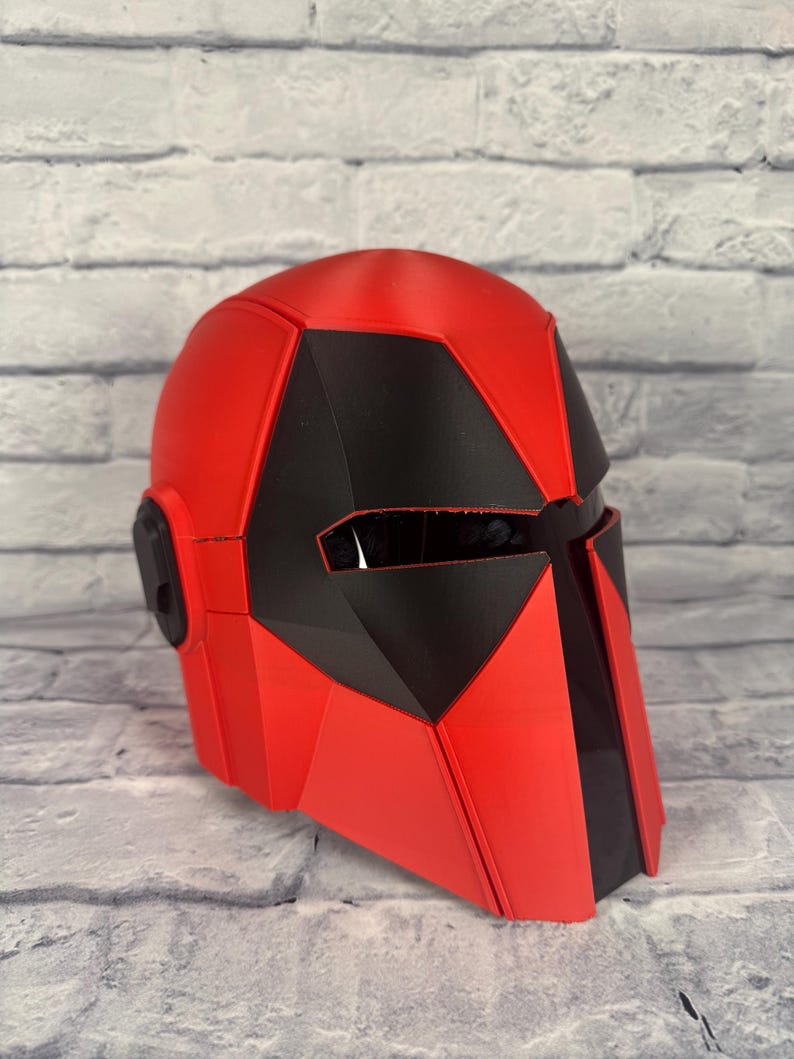 以下が含まれることがあります： 幾何学模様の赤と黒のヘルメット。ヘルメットは滑らかで光沢のある仕上がりで、黒色の顕著なバイザーエリアが特徴です。 全体的な形状は、未来的なテーマまたはSFテーマを示唆しています。