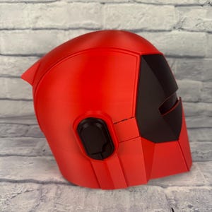 以下が含まれることがあります： 黒いバイザーとイヤーピースが付いた赤いヘルメット。ヘルメットは硬い素材でできており、滑らかな仕上がりです。 デザインは角度があり未来的で、洗練されたモダンな美学です。