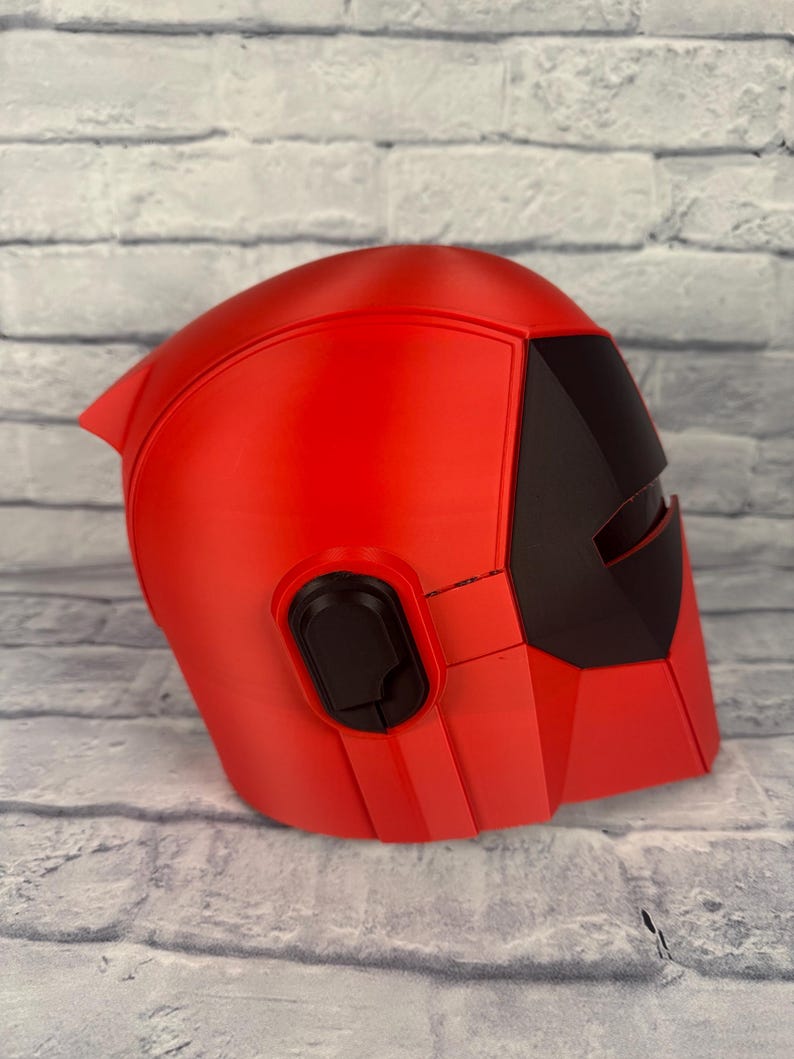 以下が含まれることがあります： 黒いバイザーとイヤーピースが付いた赤いヘルメット。ヘルメットは硬い素材でできており、滑らかな仕上がりです。 デザインは角度があり未来的で、洗練されたモダンな美学です。