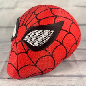 Puede incluir: M&aacute;scara de Spider-Man roja y negra con una cubierta de ojo de malla. La m&aacute;scara est&aacute; hecha de un material texturizado y tiene un dise&ntilde;o de telara&ntilde;a.