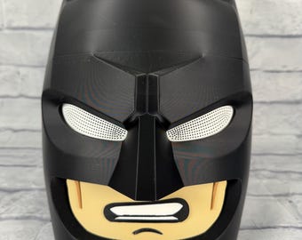 Op de afbeelding: Een zwarte Batman-hoofdcontainer met puntige oren, witte mesh ooguitsparingen en een beige onderkant van het gezicht met een geprinte mond die gebalde tanden toont, uitgevoerd in een gladde, matte afwerking met geometrische vormen.