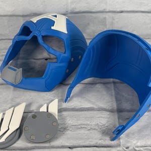 May include: Blue plastic Captain America helmet with a white A on the front. The helmet is in two pieces, one for the front and one for the back. There are also two gray and white plastic pieces with a magnetic backing.