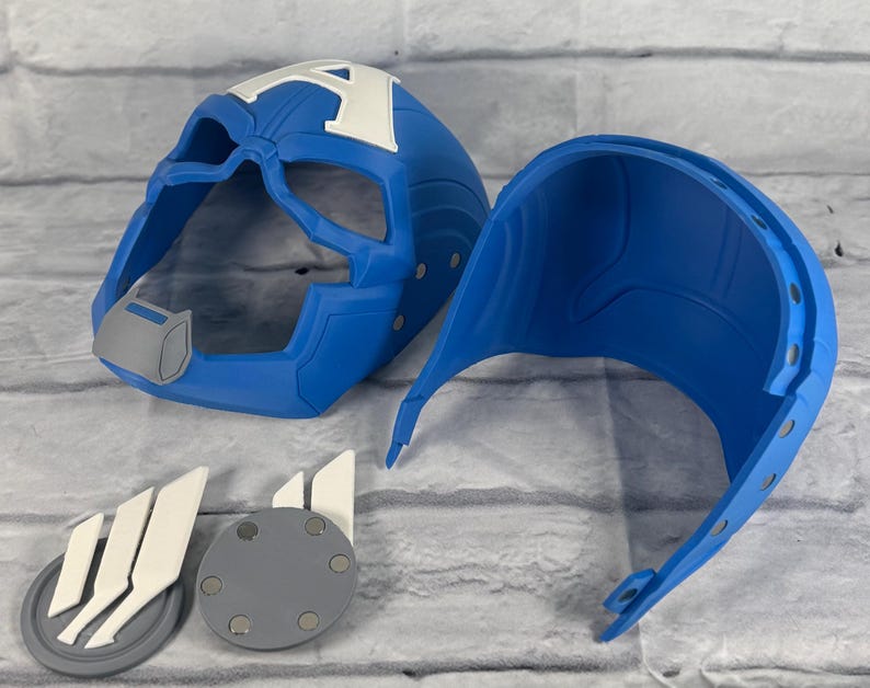 May include: Blue plastic Captain America helmet with a white A on the front. The helmet is in two pieces, one for the front and one for the back. There are also two gray and white plastic pieces with a magnetic backing.